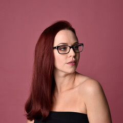Fototapeta premium Close up portrait of a red haired woman with expressive facial features and glasses on a pink studio background.