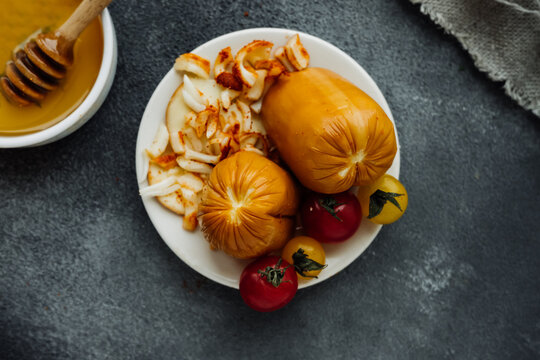 smoked cheese with crust, cheese crumbs and cherry tomatoes on dark table with bowl of honey and wooden stick. types of cheese, cooking products from milk at home, selective focus