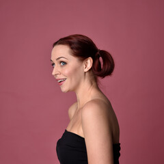 Close up portrait of a red haired woman with expressive facial features on a pink studio background.