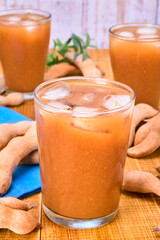glass of tamarind water with ice cubes and whole tamarinds on the side. traditional mexican drink...