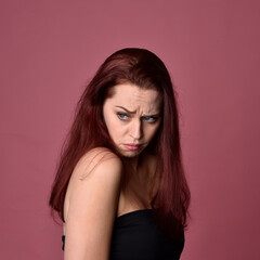 Close up portrait of a red haired woman with expressive facial features on a pink studio background.