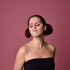 Close up portrait of a red haired woman with expressive facial features on a pink studio background.