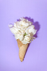 A bouquet of white roses instead of ice cream in a waffle cone on a purple background. Creative minimalism