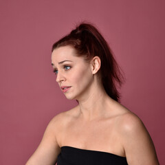 Close up portrait of a red haired woman with expressive facial features on a pink studio background.