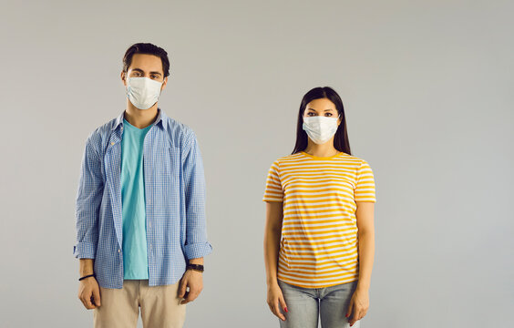 Studio portrait of two people wearing surgical face masks. Young couple with medical face masks covering mouths standing on light gray background. Health protection during coronavirus pandemic concept