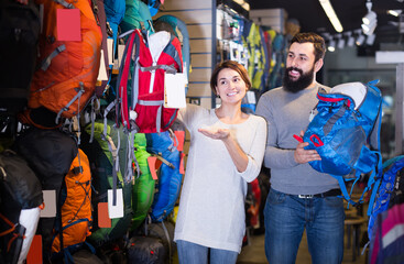 attentive couple examining various rucksacks in sports equipment store