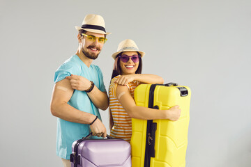 Young people ready for safe summer holiday journey. Studio portrait of happy couple holding travel cases, smiling and showing arms after receiving COVID-19 vaccine. Coronavirus vaccination concept - obrazy, fototapety, plakaty