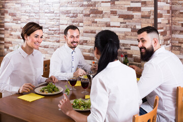 group of laughing friends eating at restaurant table and chatting