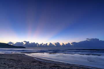 Sunrise at the seaside with low cloud bank and early sun rays during blue hour