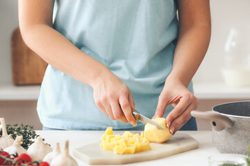 Woman cutting potato on table in kitchen