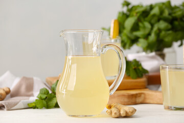 Jug of healthy ginger juice on light wooden background