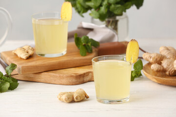 Glass of healthy ginger juice on light wooden background