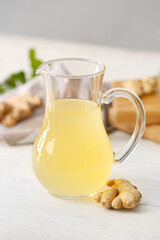 Jug of healthy ginger juice on light wooden background