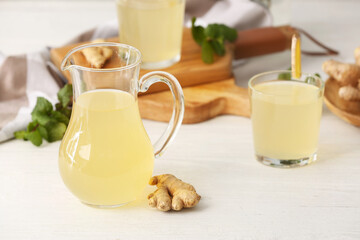 Jug of healthy ginger juice on light wooden background