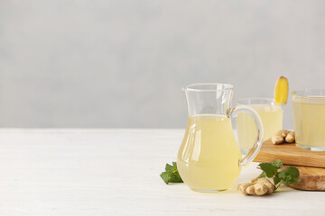 Jug of healthy ginger juice on light wooden background