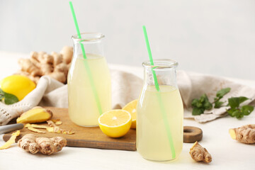 Bottles of healthy ginger juice on light background