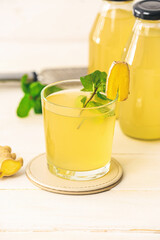 Glass of healthy ginger juice on light wooden background