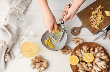 Woman grating ginger on white wooden background