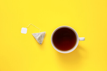 Cup of hot beverage and tea bag on color background