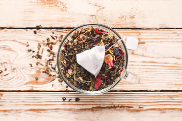 Cup with tea bag and dry leaves on light wooden background