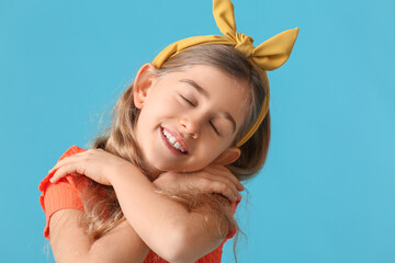 Little girl embracing herself on color background