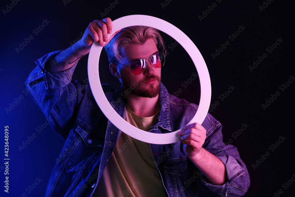 Wall mural Toned portrait of handsome young man with neon lamp on dark background