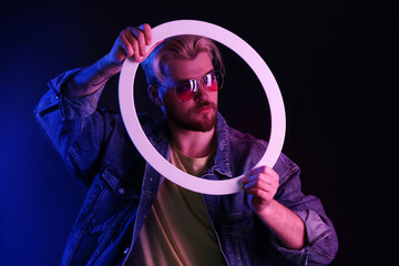 Toned portrait of handsome young man with neon lamp on dark background