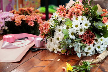 A bouquet of multi-colored chrysanthemums lies on a wooden table. The process of making a bouquet of flowers by a florist.
