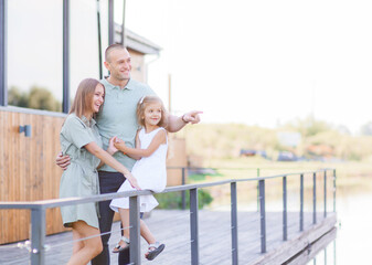 Happy parents with child standing on balcony of house, laughing, looking at something