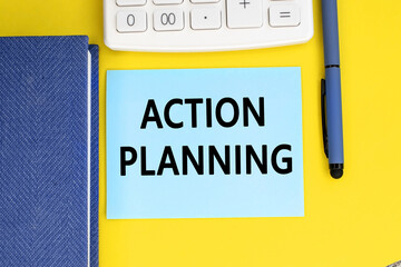 The label action planning is on a sheet that lies on a yellow background next to a white calculator and a blue notebook with a pen.