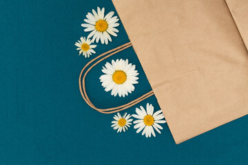 Paper bag on a blue background, decorated with daisies, brown shopping bag. Craft bag with handle. Packaging template mockup. Delivery service concept. Copy space