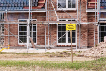 Fototapeta na wymiar Vor einem fast fertigen Einfamilienhaus steht ein Schild mit der Aufschrift Baustelle Betreten verboten