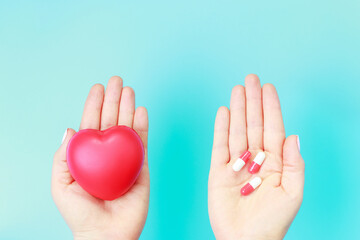 A female hands holding heart shape and medical capsules top view.