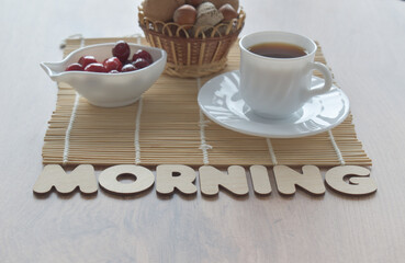 Inscription in wooden letters - morning. White mug with coffee, nuts, red berries. Light morning breakfast concept.