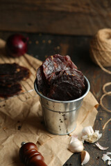 Homemade beef jerky seasoned with garlic, onion, pepper and salt. Jerky in a bucket on a wooden background