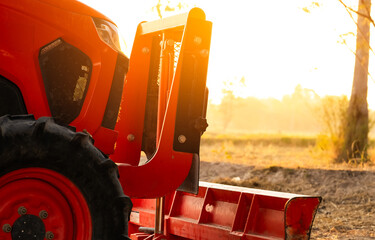 Orange tractor parked at rice farm in summer morning with sunlight. Agricultural machinery in...