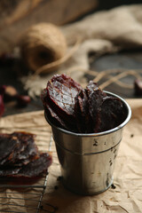 Homemade beef jerky seasoned with garlic, onion, pepper and salt. Jerky in a bucket on a wooden...