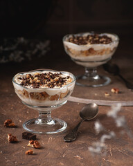 Dessert with yoghurt cream, chocolate and nuts in glass bowls on a dark brown stone background
