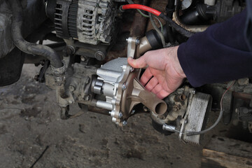 Car mechanic replacing water pump at modern common rail diesel engine, closeup of workers  hand holding part