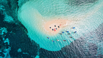 View from above or from a bird's eye view of the coral island, the white sand beach and the beautiful, clear turquoise waves with boats.