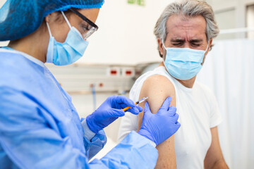 Fototapeta premium Professional doctor or nurse giving flu or COVID-19 injection to patient. Man in medical face mask getting antiviral vaccine at hospital or health center during vaccination and immunization campaign