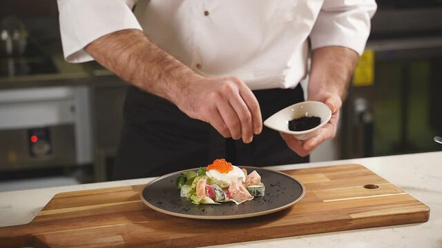 The chef sprinkles seasoning on the original salad with poached egg, salmon and red caviar, vegetable salad