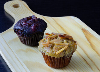 Banana cupcake and chocolate muffin on wooden tray.