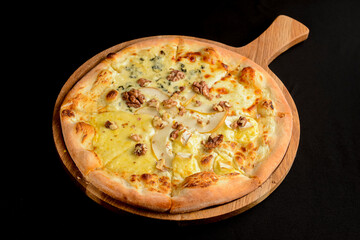 Sliced Pizza with pear, gorgonzola and nuts served on a wooden board over black background.
