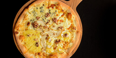 Sliced Pizza with pear, gorgonzola and nuts served on a wooden board over black background.