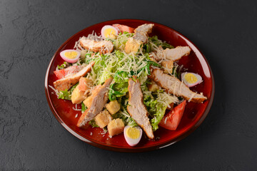 Red plate of Caesar Salad over black background. Traditional Italian cuisine concept, traditional recipe.