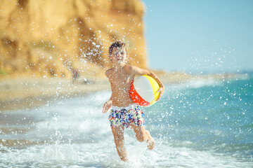 Boy child has fun at sea. Summer, happiness, sea and a child with a ball. High quality photo.