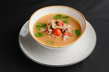 Mushroom soup of chicken broth, mushrooms, cherry tomato served in a white bowl over black background.