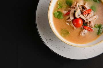 Mushroom soup of chicken broth, mushrooms, cherry tomato served in a white bowl over black background.