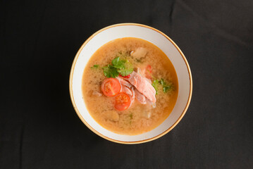 Vegetable soup with salmon in white bowl over black background. Dinner concept, healthy hot soup.
